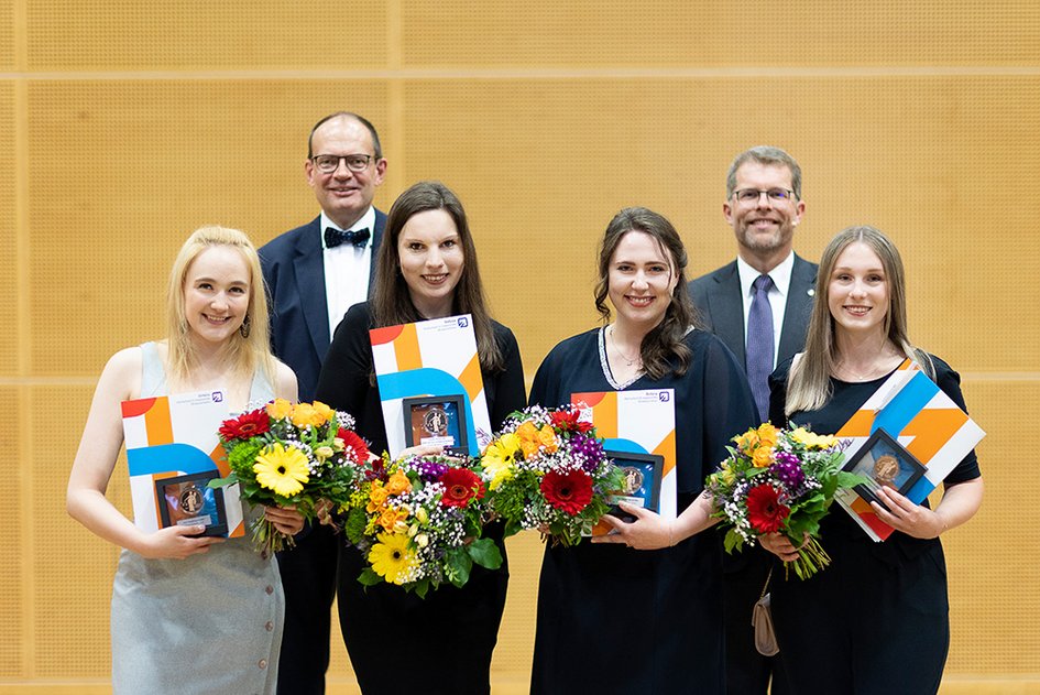 Vier Preisträgerinnen halten ihre Auszeichnungen und Blumensträuße in den Händen, in der zweiten Reihe stehen Dekan und Studiendekan.