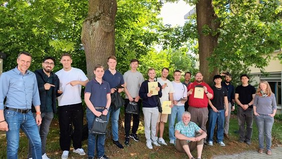 Eine gemischte Gruppe aus 15 Personen posiert vor einem Hintergrund voller Bäume.