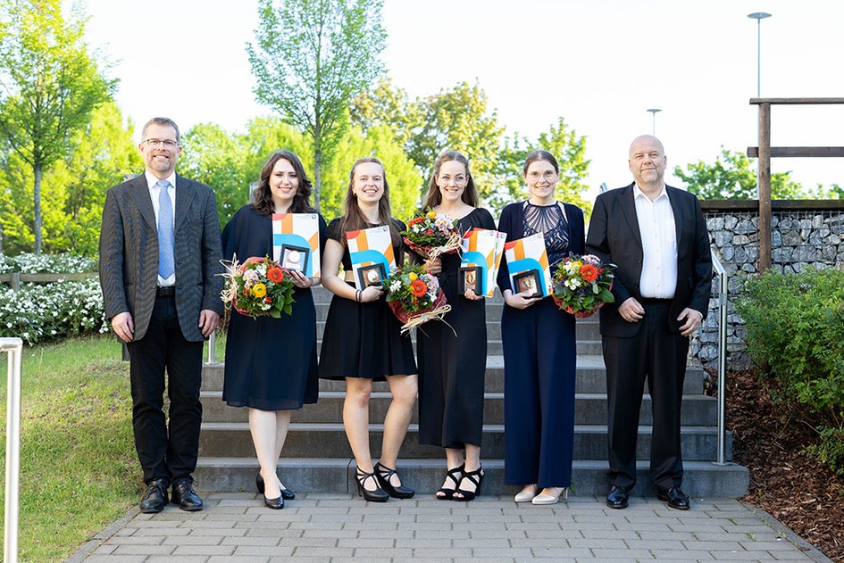 Die vier Preisträgerinnen mit ihren Auszeichnungen und Blumensträußen in den Händen auf der Treppe zwischen Gebäude K und Gebäude R.