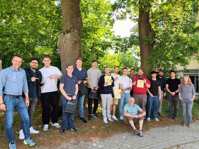 Eine gemischte Gruppe aus 15 Personen posiert vor einem Hintergrund voller Bäume.